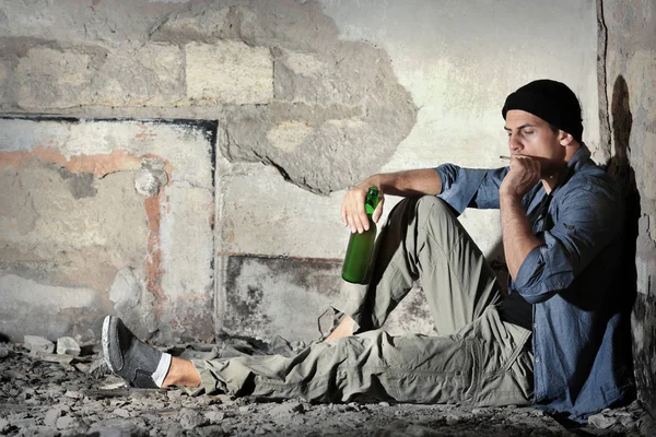 タバコと断念された建物にアルコールのボトルに座っている男 — ストック写真