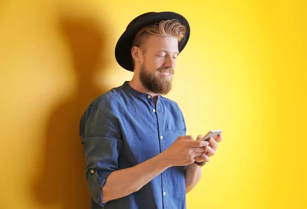 Homem jovem hipster usando smartphone no fundo de cor — Fotografia de Stock