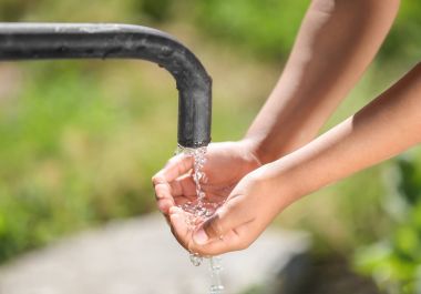 African American child drinking water from tap outdoors. Water scarcity concept clipart