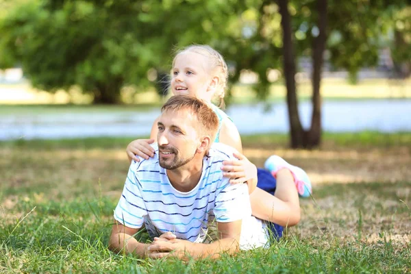 Jonge man met klein meisje liggen op gras in park — Stockfoto