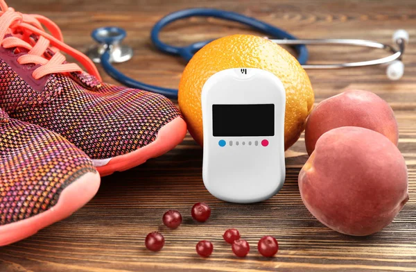 Komposition mit digitalem Glukometer, Früchten und Turnschuhen auf Holzgrund. Diabetes-Konzept — Stockfoto