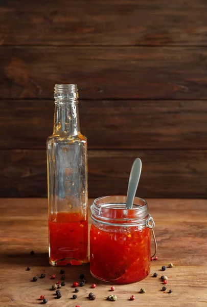 Glass jar and bottle with chili sauce on wooden background — Stock Photo, Image