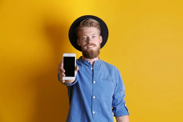 Jovem hipster homem segurando smartphone no fundo de cor — Fotografia de Stock