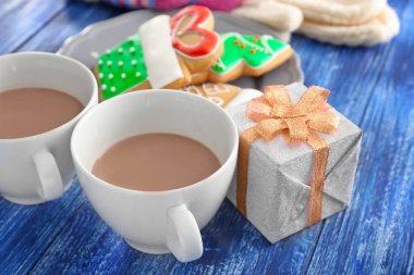 Bardak sıcak çikolata, hediye kutusu ve renk ahşap arka plan üzerinde Noel kurabiyeleri