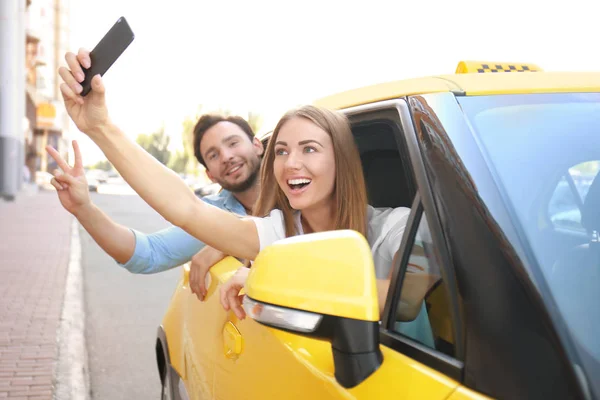 Młoda para biorąc selfie siedząc w samochodzie taxi — Zdjęcie stockowe