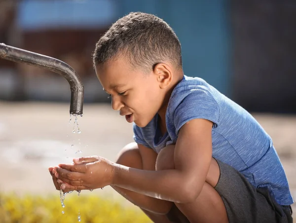 アフリカ系アメリカ人の子供は屋外の蛇口から水を飲む。水の希少性の概念 — ストック写真