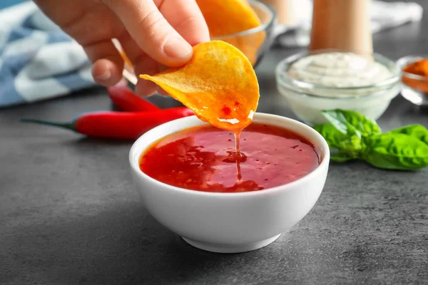Person dipping potato chip in chili sauce indoors — Stock Photo, Image