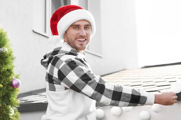Man in Santa hat decorating facade of house with garland for Christmas — Stock Photo, Image