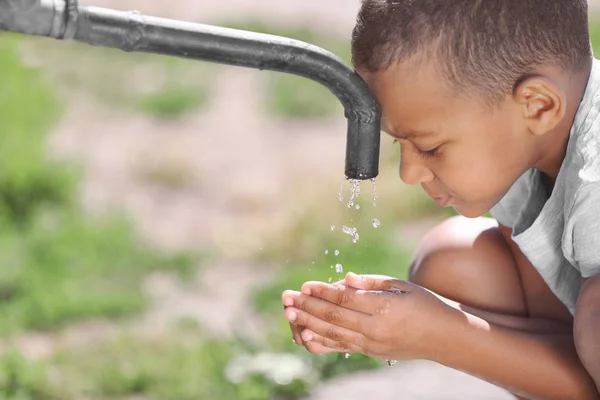 African American child drinking water from tap outdoors. Water scarcity concept