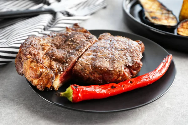 Cut steak with chili pepper on black plate — Stock Photo, Image