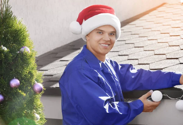 Ο άνθρωπος με το καπέλο Σάντα διακόσμηση πρόσοψη του σπιτιού με γιρλάντα για τα Χριστούγεννα — Φωτογραφία Αρχείου