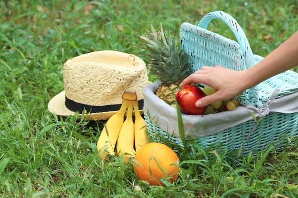 Mão tomando frutas de cesta de piquenique no parque — Fotografia de Stock