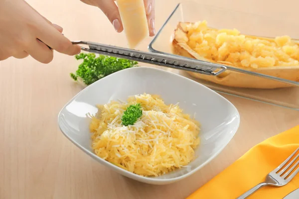 Woman grating cheese on spaghetti squash in plate — Stock Photo, Image