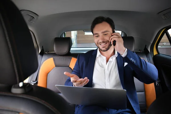 Taksi arabada otururken telefonda konuşurken laptop ile yakışıklı adam — Stok fotoğraf