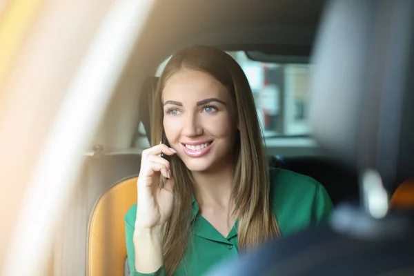 Kaunis nainen puhuu puhelimessa istuessaan taksissa — kuvapankkivalokuva