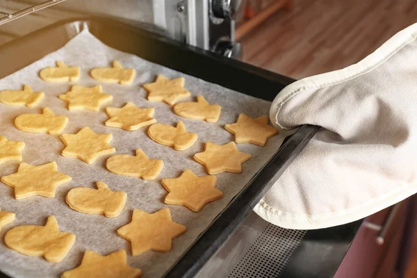 Hand einer Frau legt Backblech mit rohen Plätzchen in den Ofen — Stockfoto