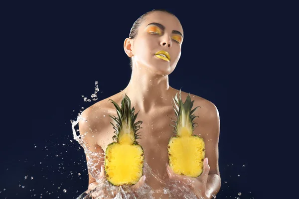 Stänk vatten på kvinna med ljusa smink och ananas halvor på mörk bakgrund — Stockfoto