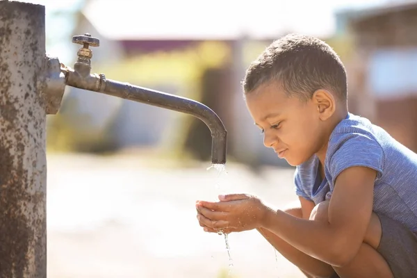 Afrikanisches amerikanisches Kind trinkt Wasser aus dem Wasserhahn im Freien. Wasserknappheitskonzept — Stockfoto