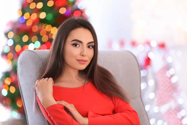 屋内でぼやけたクリスマス背景に肘掛け椅子に座って魅力的な若い女性 — ストック写真