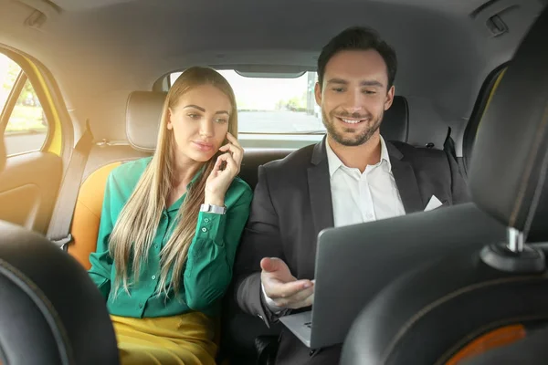 Mulher bonita falando no telefone e homem bonito com laptop sentado no banco de trás no carro de táxi — Fotografia de Stock