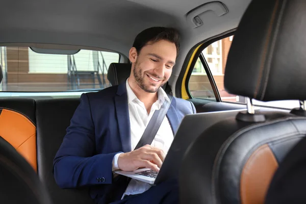 Bonito homem com laptop sentado em carro de táxi — Fotografia de Stock