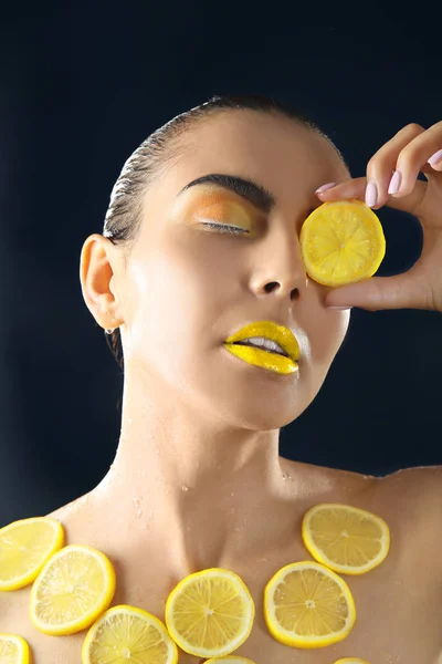 Kvinna med citronskivor på mörk bakgrund — Stockfoto