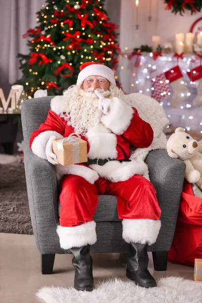 Authentic Santa Claus with gift box sitting in armchair at room decorated for Christmas — Stock Photo, Image