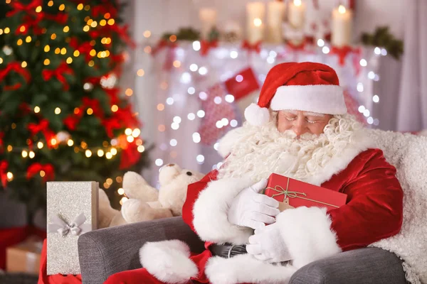 Authentische Weihnachtsmann mit Geschenkbox sitzt im Sessel in Zimmer für Weihnachten dekoriert — Stockfoto