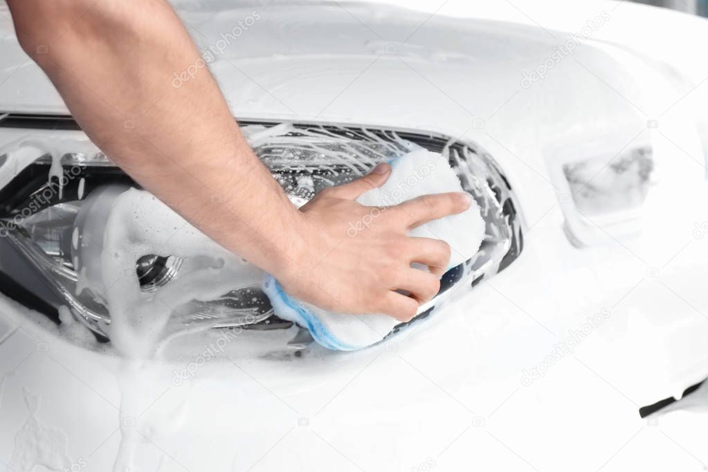 Man washing automobile headlight with sponge, closeup
