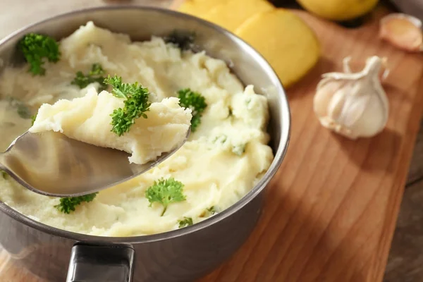 Spoon with mashed potatoes over sauce pan, closeup