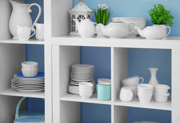 Белый стенд хранения с керамической посудой на цветном фоне — стоковое фото