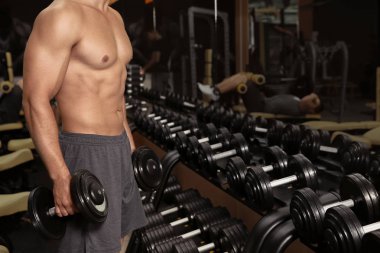 Spor salonunda dumbbells ile egzersiz yaparak sportif genç adam