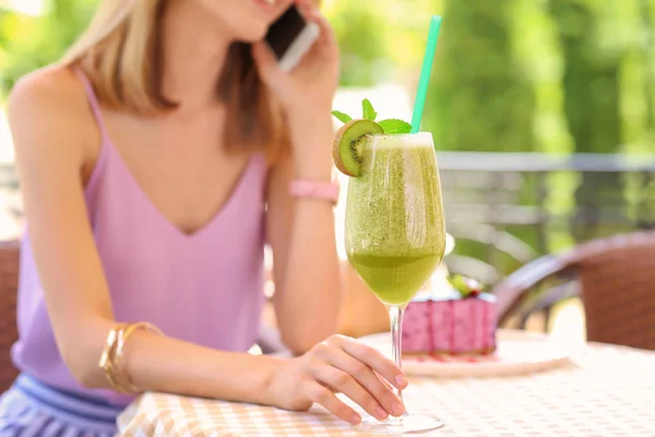 Mooie jonge vrouw met verse smoothie praten op mobiele telefoon in café — Stockfoto