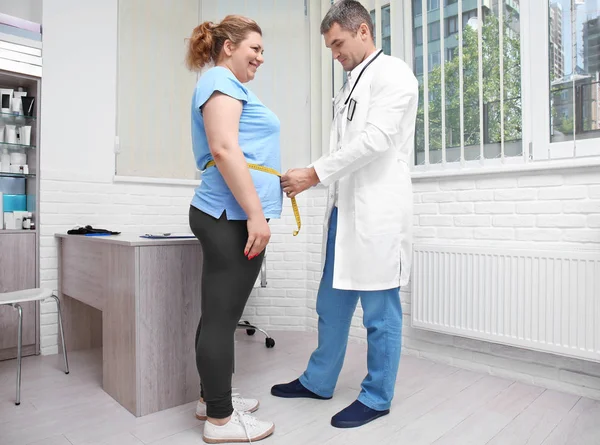 Male doctor measuring waist of overweight woman in hospital — Stock Photo, Image