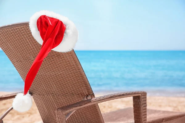 Cama de sol vazia com chapéu de Papai Noel na praia perto do mar. Natal feriados conceito — Fotografia de Stock