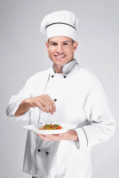Chef macho joven sosteniendo plato con ensalada sobre fondo claro — Foto de Stock