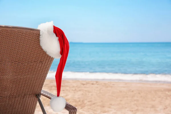 Cama de sol vazia com chapéu de Papai Noel na praia perto do mar. Natal feriados conceito — Fotografia de Stock