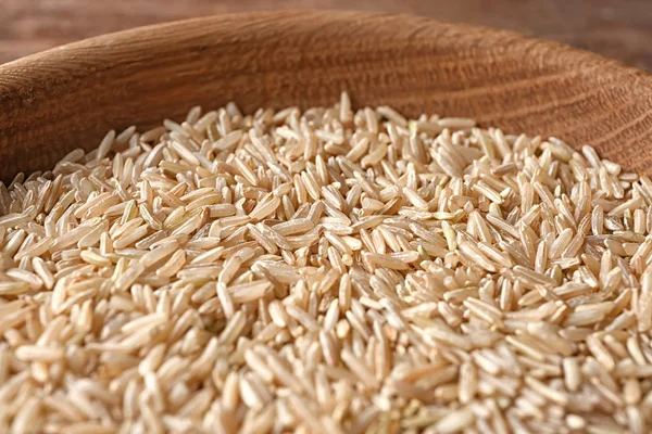 Wooden plate with raw brown rice — Stock Photo, Image