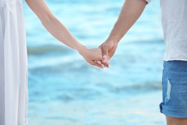 Deniz kıyısında el ele tutuşan mutlu genç çift