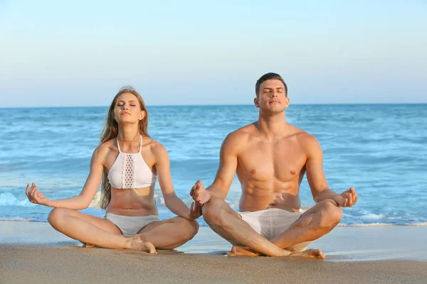 Giovane coppia che pratica yoga sulla spiaggia di mare — Foto Stock