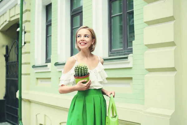 Молодая счастливая хипстерша в зеленой юбке держит кактус на улице — стоковое фото
