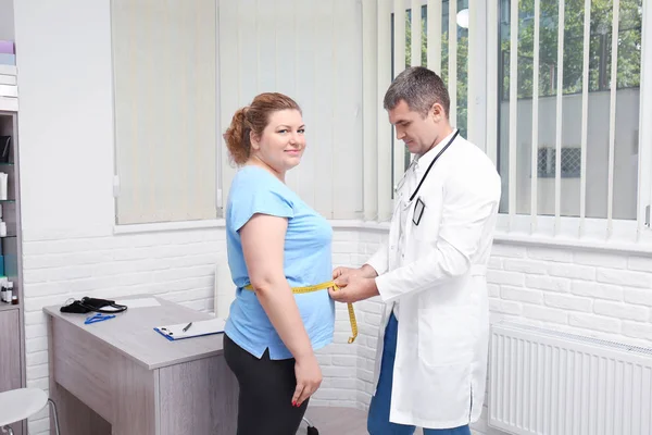 Мужчина, измеряющий талию женщины с избыточным весом в больнице — стоковое фото
