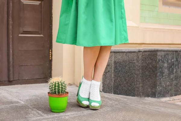 Hipster vrouw in groene rok staande in de buurt van cactus buitenshuis — Stockfoto