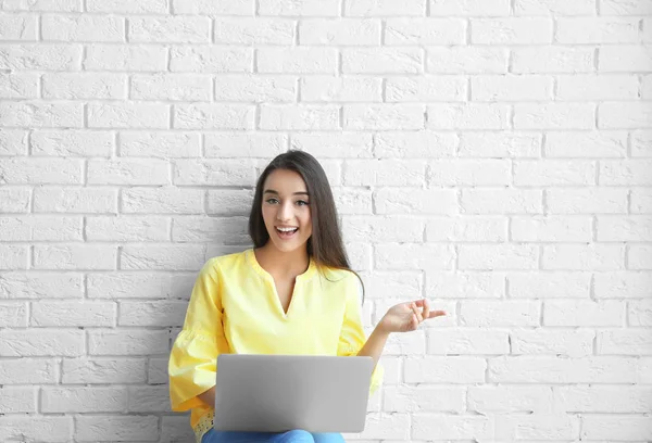 Young female blogger with laptop on brick wall background — Stock Photo, Image