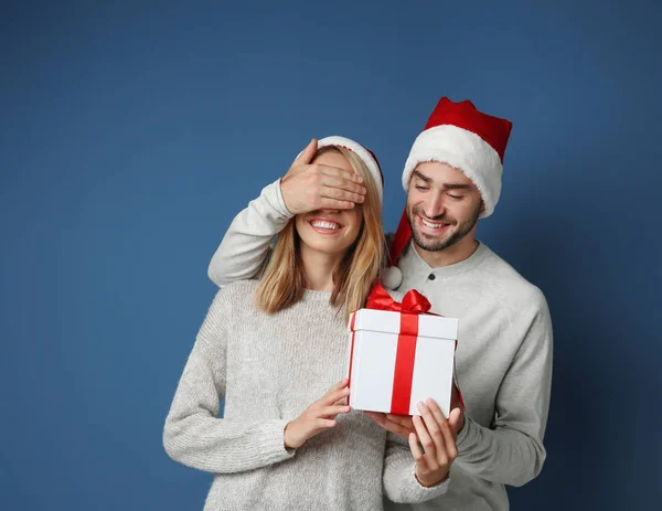 Joven hombre dando a su novia regalo de Navidad, sobre fondo de color —  Fotos de Stock