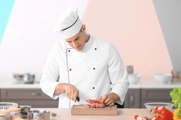 Giovane chef maschio che taglia carne su tavola di legno in cucina — Foto Stock