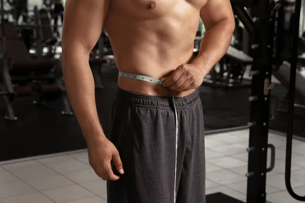 Jeune homme sportif avec ruban à mesurer dans la salle de gym — Photo