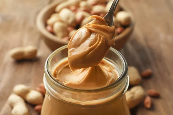 Spoon and glass jar with creamy peanut butter — Stock Photo, Image