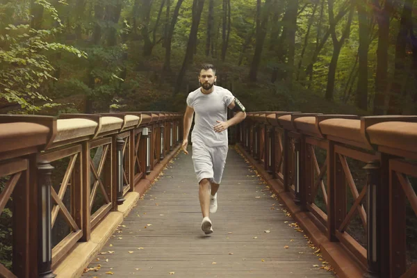 Спортивный человек бежит по мосту в парке — стоковое фото