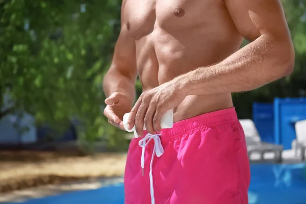 スイミング プールの近くの皮膚の上に日焼け止めを適用する魅力的な男性 — ストック写真